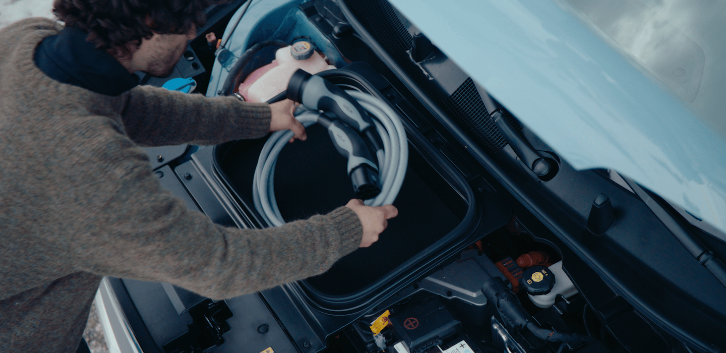 Nahaufnahme einer Person, die ein Ladekabel aus seinem Ablagefach unter der Motorhaube eines elektrischen Kias nimmt.